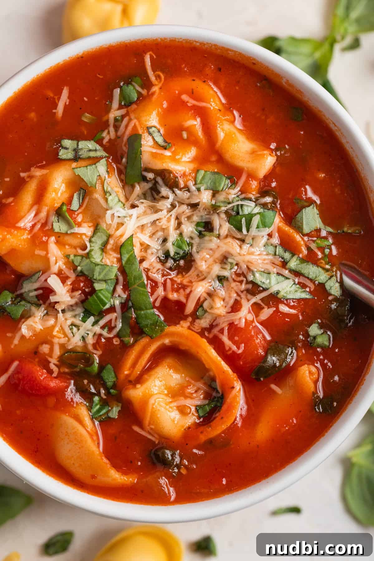 Creamy Tomato Tortellini Soup Recipe for Cozy Dinners 2 White bowl of tomato tortellini soup topped with fresh parmesan and chopped basil.