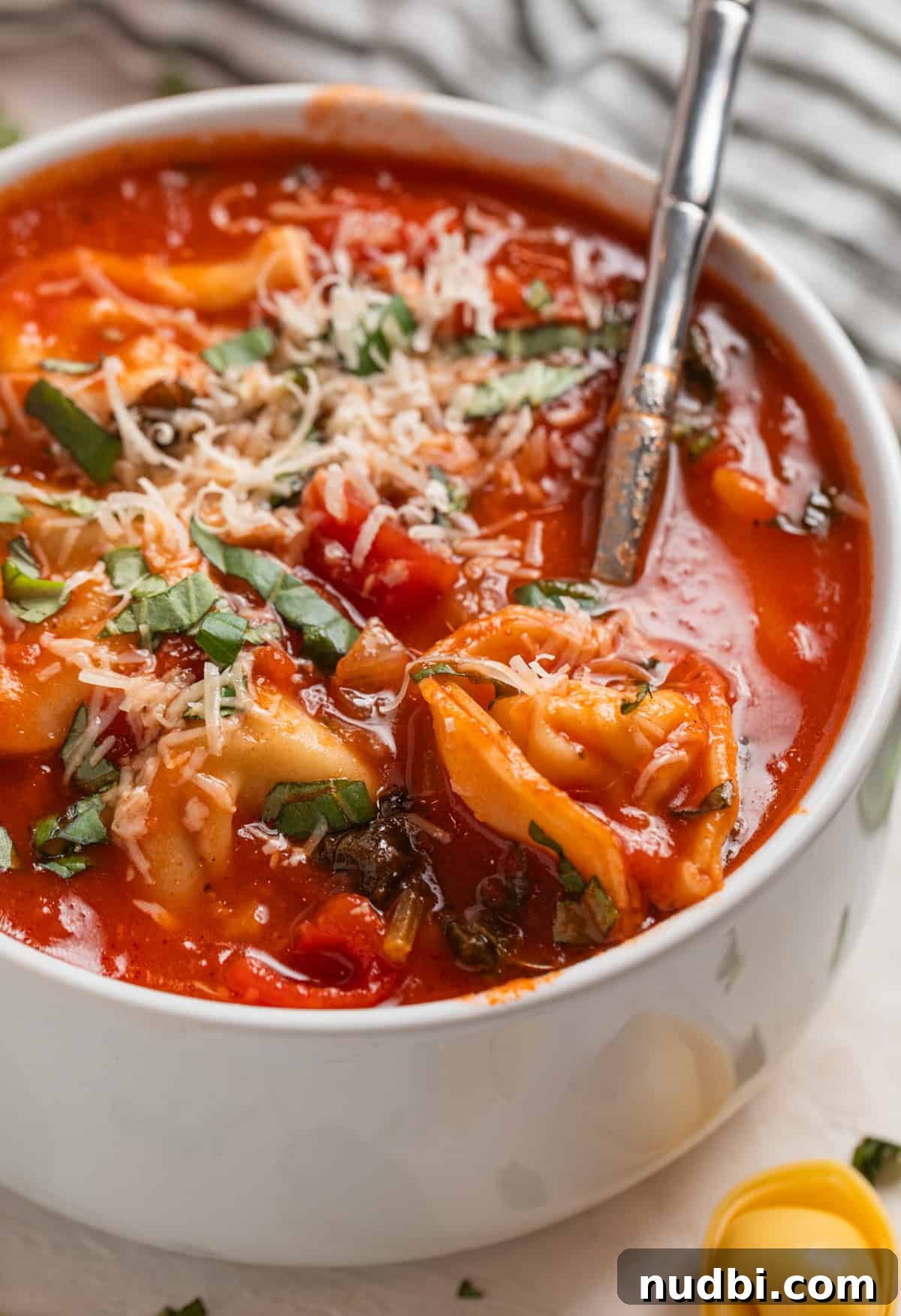 Creamy Tomato Tortellini Soup Recipe for Cozy Dinners 6 Spoon scooping in soup with tortellini topped with parmesan and basil in spoon.