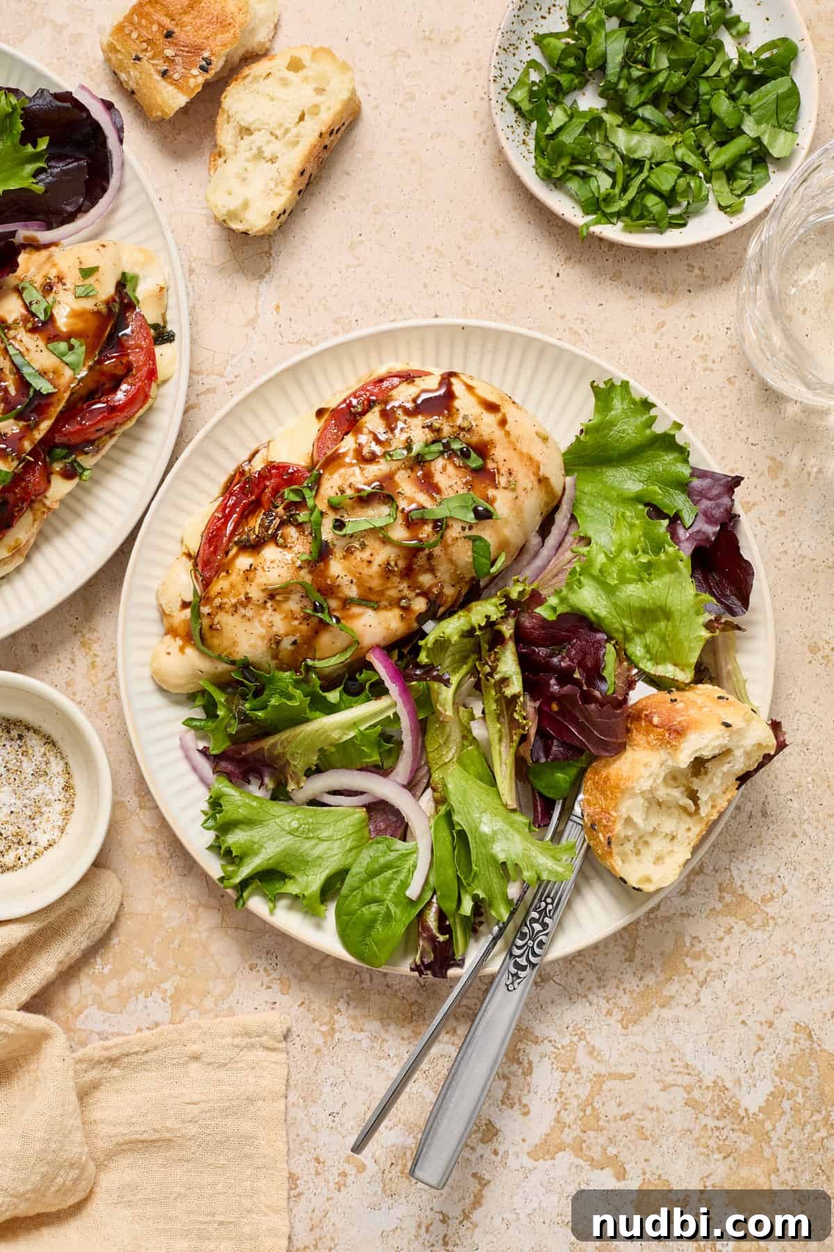 Mozzarella-Stuffed Chicken Breasts with Garlic Herb Pan Sauce 12 Plate with chicken, salad and piece of bread with fork and knife placed on side of plate.