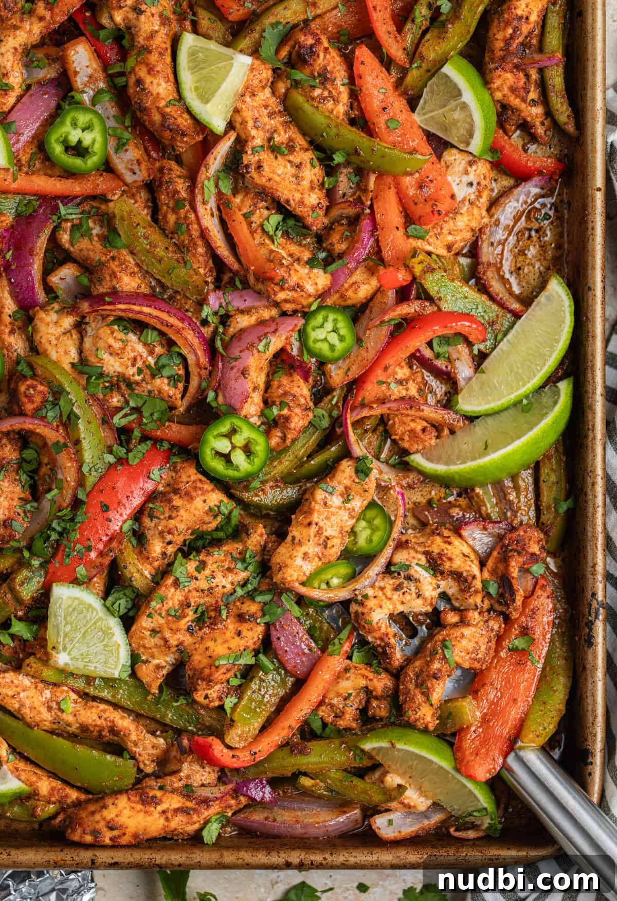 Honey-Lime Baked Chicken Fajitas Recipe for Flavorful Weeknights 2 Baked chicken fajitas on sheet pan with onions and peppers, topped with chopped cilantro, lime wedges and jalapeños.