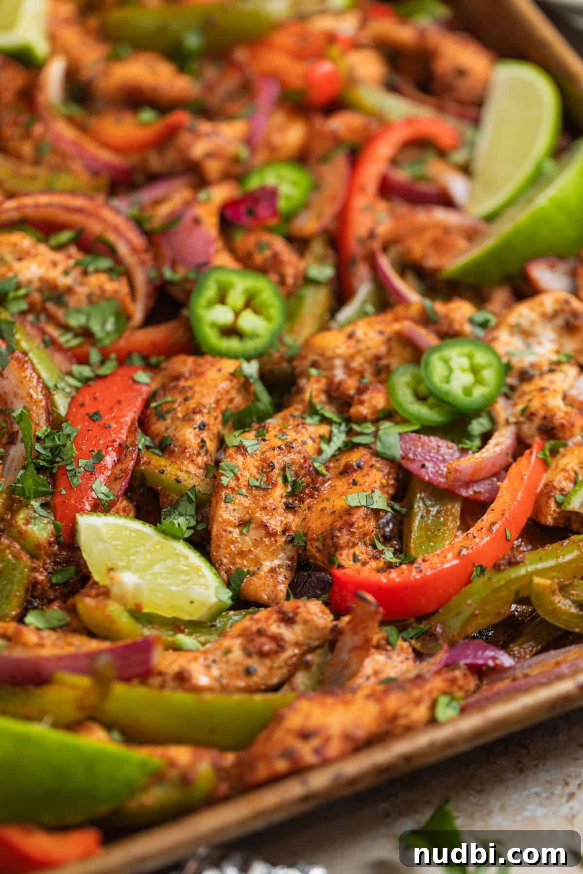 Honey-Lime Baked Chicken Fajitas Recipe for Flavorful Weeknights 3 Sheet pan with baked honey lime chicken fajitas with red onion, bell peppers and topped with chopped cilantro.