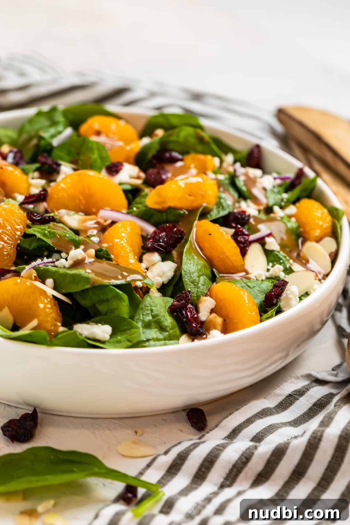 Spinach and Mandarin Salad with Honey Balsamic Vinaigrette 3 Spinach salad with mandarins, dried cranberries, toasted almonds, onion and goat cheese in white bowl.