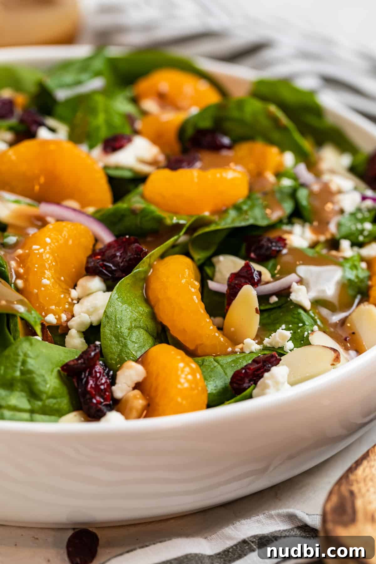 Spinach and Mandarin Salad with Honey Balsamic Vinaigrette 4 White bowl with spinach, mandarin oranges, almonds and more with wood spoon beside it.