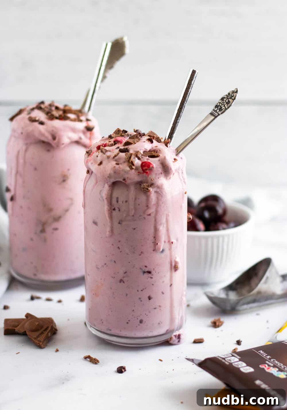 Decadent Chocolate Cherry Milkshake Recipe 3 Cherry milkshake in glasses with ice cream scoop and bowl of cherries behind.