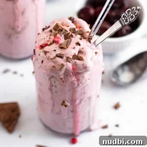 Decadent Chocolate Cherry Milkshake Recipe 4 Cherry Milkshake with chocolate chunks in glass with bowl of cherries.