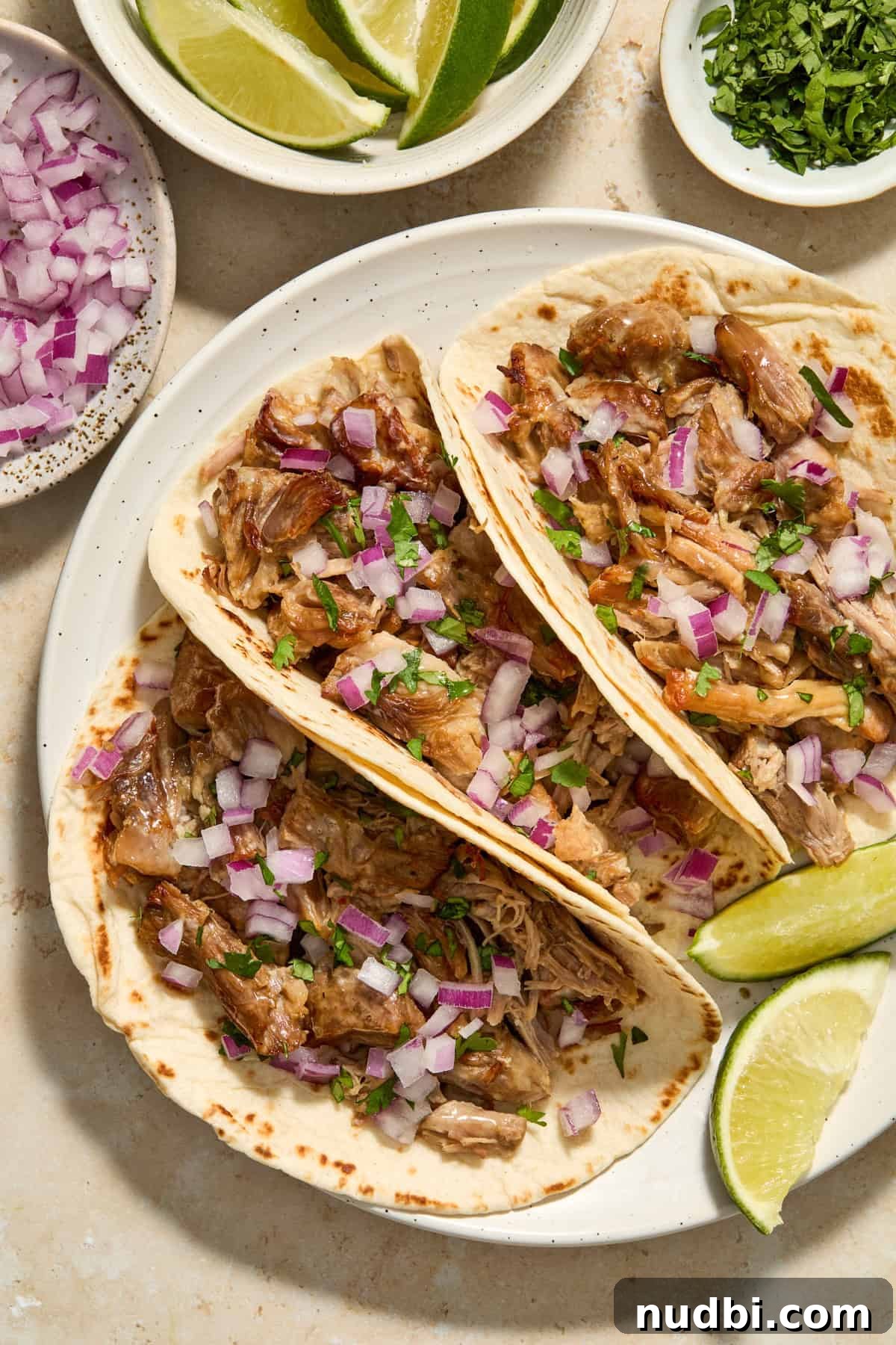 Crispy Instant Pot Carnitas Recipe for Tender, Crunchy Pork 2 Pork carnitas in tortillas topped with diced red onion and chopped cilantro.