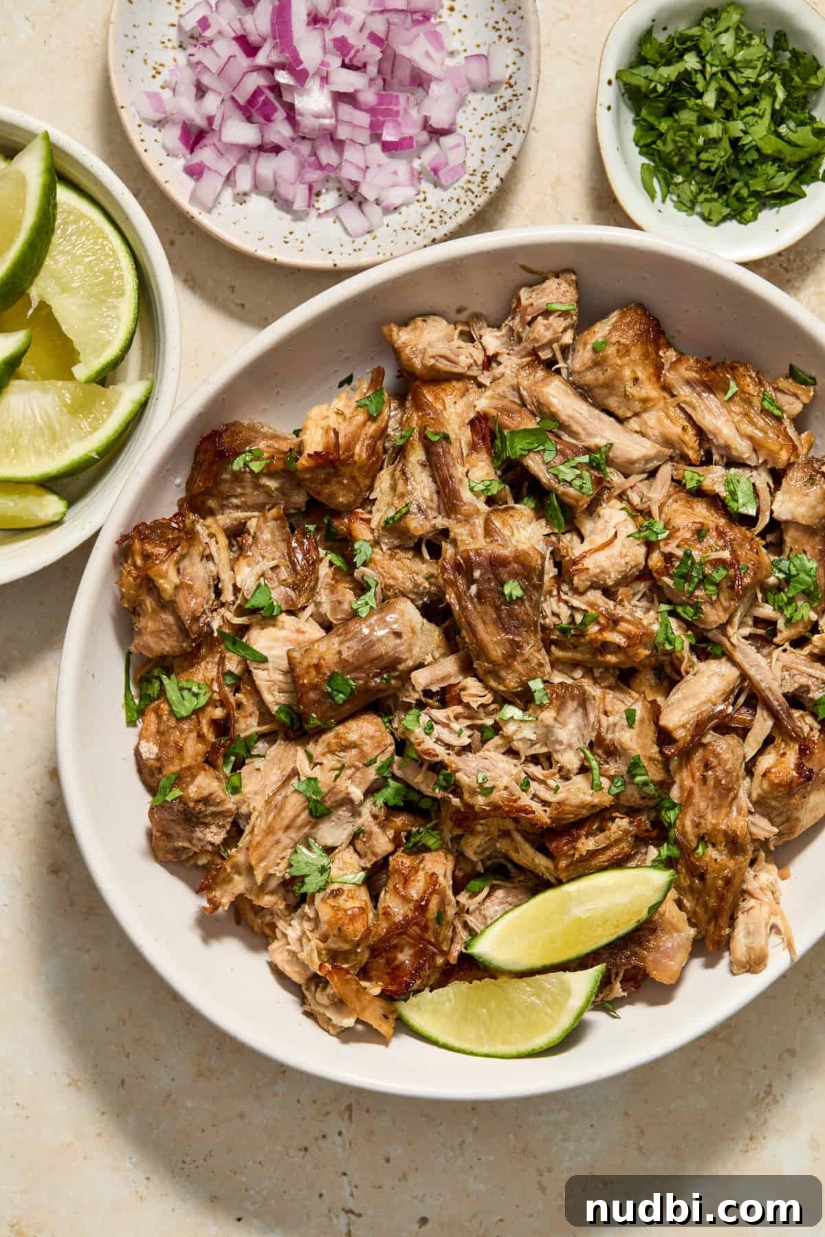 Crispy Instant Pot Carnitas Recipe for Tender, Crunchy Pork 10 Bowl with shredded pork carnitas meat topped with cilantro and bowls of limes, onions and cilantro surrounding.