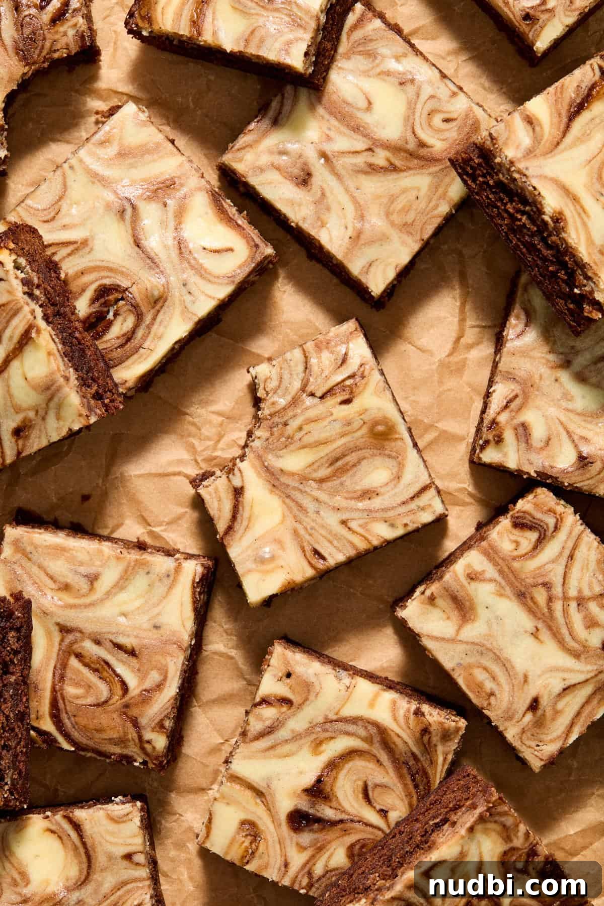 Kahlúa Cream Cheese Brownies Recipe — Luscious Coffee-Chocolate Swirl 2 Kahlua brownies cut and arranged on parchment with bite taken out of center brownie.