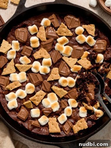 Brownie in skillet topped with marshmallows, chocolate bars and pieces of graham crackers.
