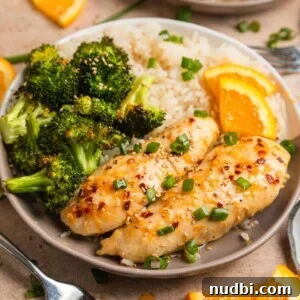 Sticky Orange Sheet Pan Chicken Dinner 11 Baked orange chicken sheet pan dinner served on plate with white rice and orange slices.