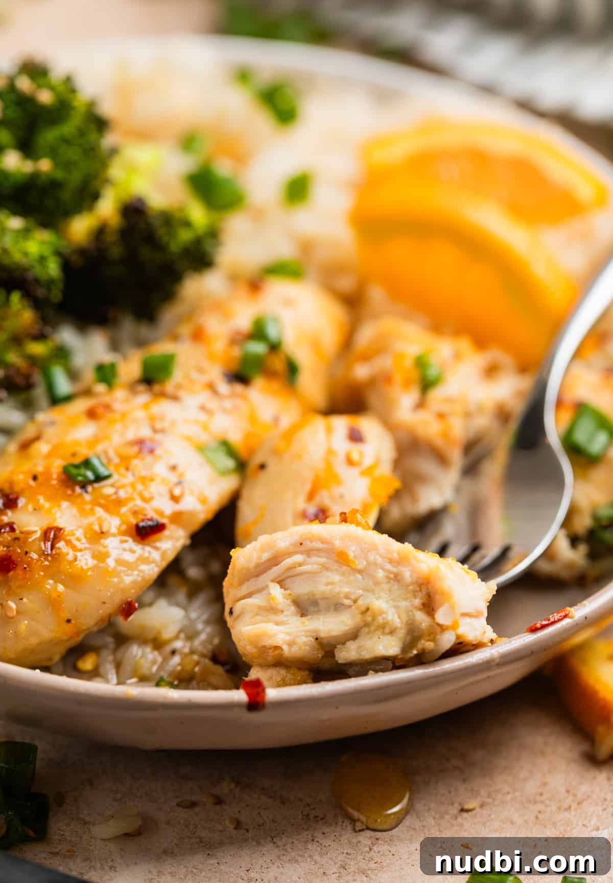 Sticky Orange Sheet Pan Chicken Dinner 3 Piece of baked orange chicken on fork with plate of broccoli and rice.