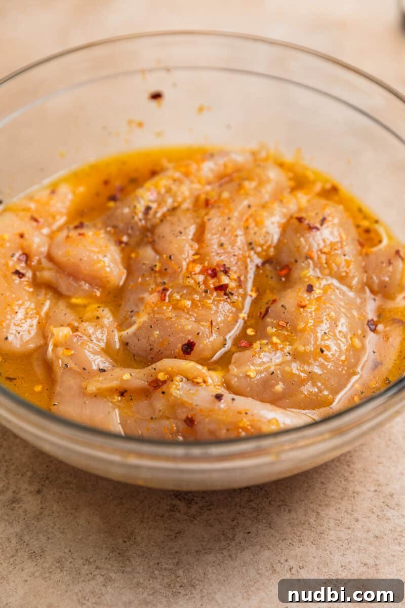 Sticky Orange Sheet Pan Chicken Dinner 6 Chicken tenderloins marinating in glass bowl with honey orange marinade.