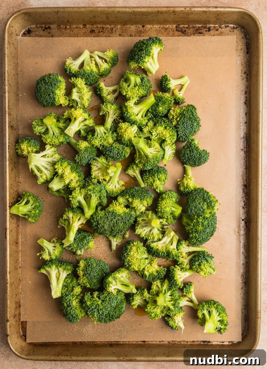 Sticky Orange Sheet Pan Chicken Dinner 7 Broccoli on parchment lined baking sheet tossed in olive oil and seasoning.