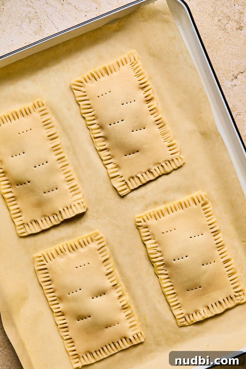 Homemade Pop-Tarts Made with Flaky Pie Crust — Sweet Breakfast Pastry 13 Holes poked into the tops of pie crust for hand pastries on baking sheet.