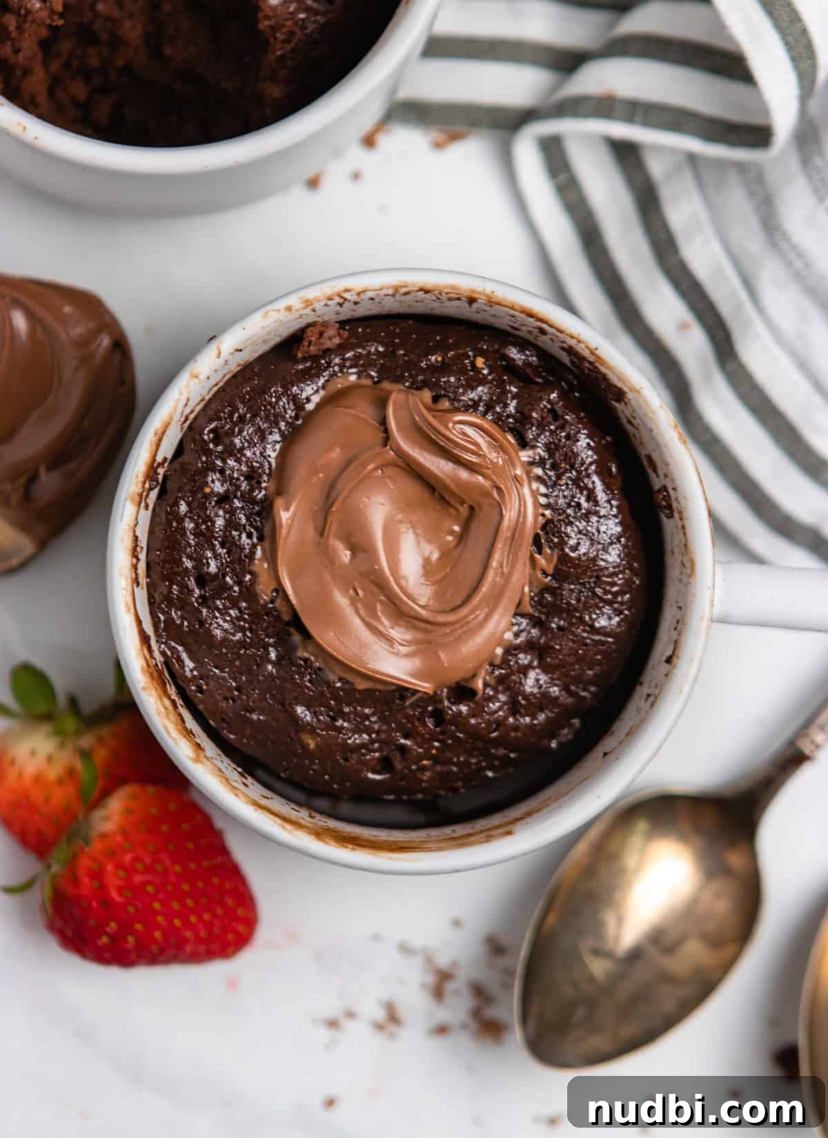 Quick Nutella Mug Cake Recipe for a Warm Chocolate Treat 2 Overhead view of nutella chocolate cake in mug with strawberries and spoon.
