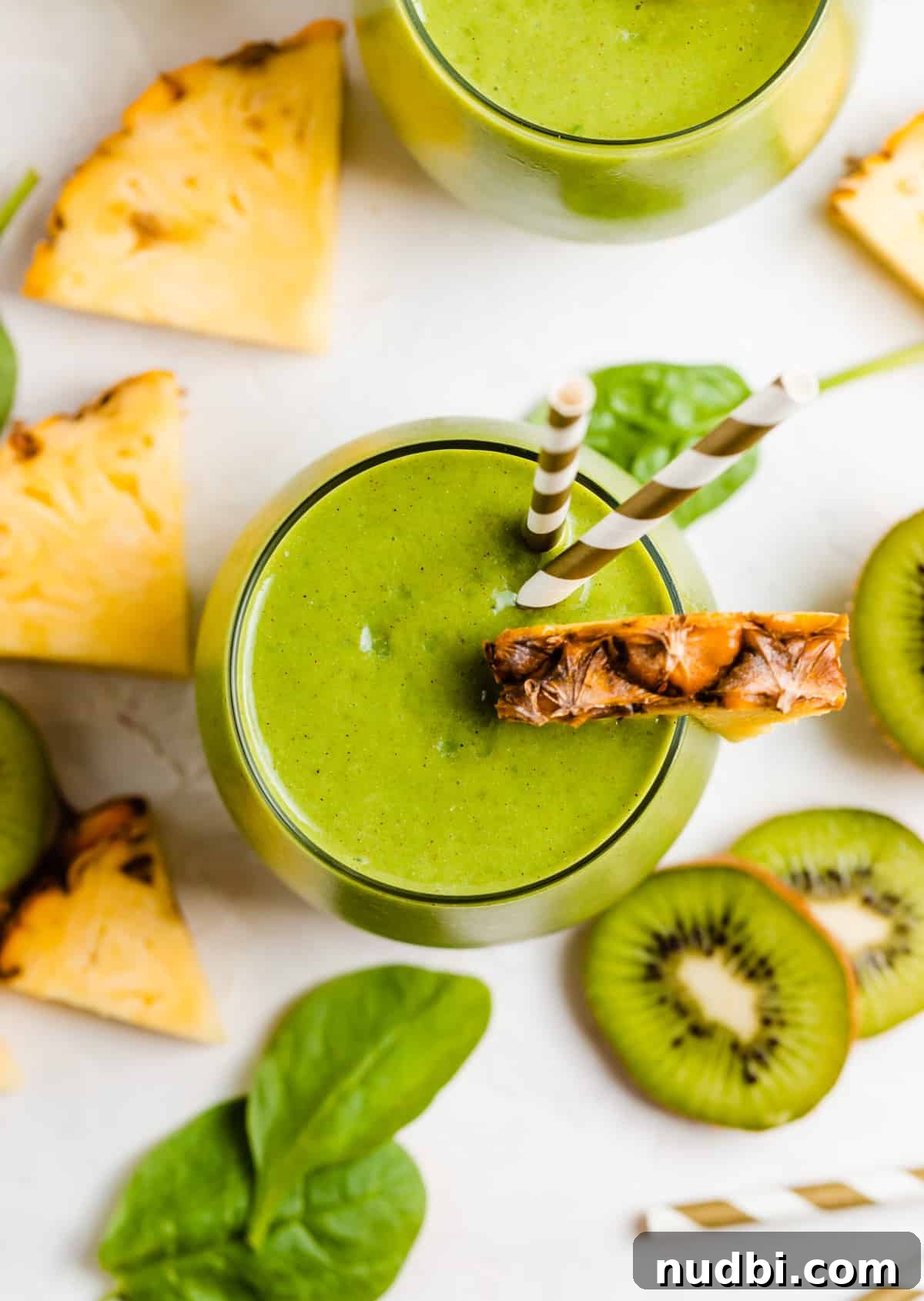 Pineapple Kiwi Smoothie Recipe for Fresh Morning Energy 5 Green kiwi pineapple smoothie in glass with pineapple and kiwi slices surrounding.