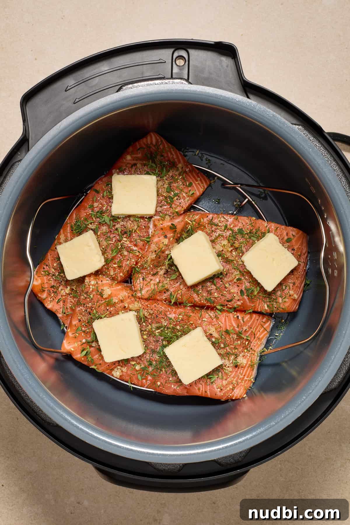 Instant Pot Butter Herb Salmon Recipe for Tender, Flaky Fish 6 Pressure cooker pot with salmon that has fresh herbs and butter on top.