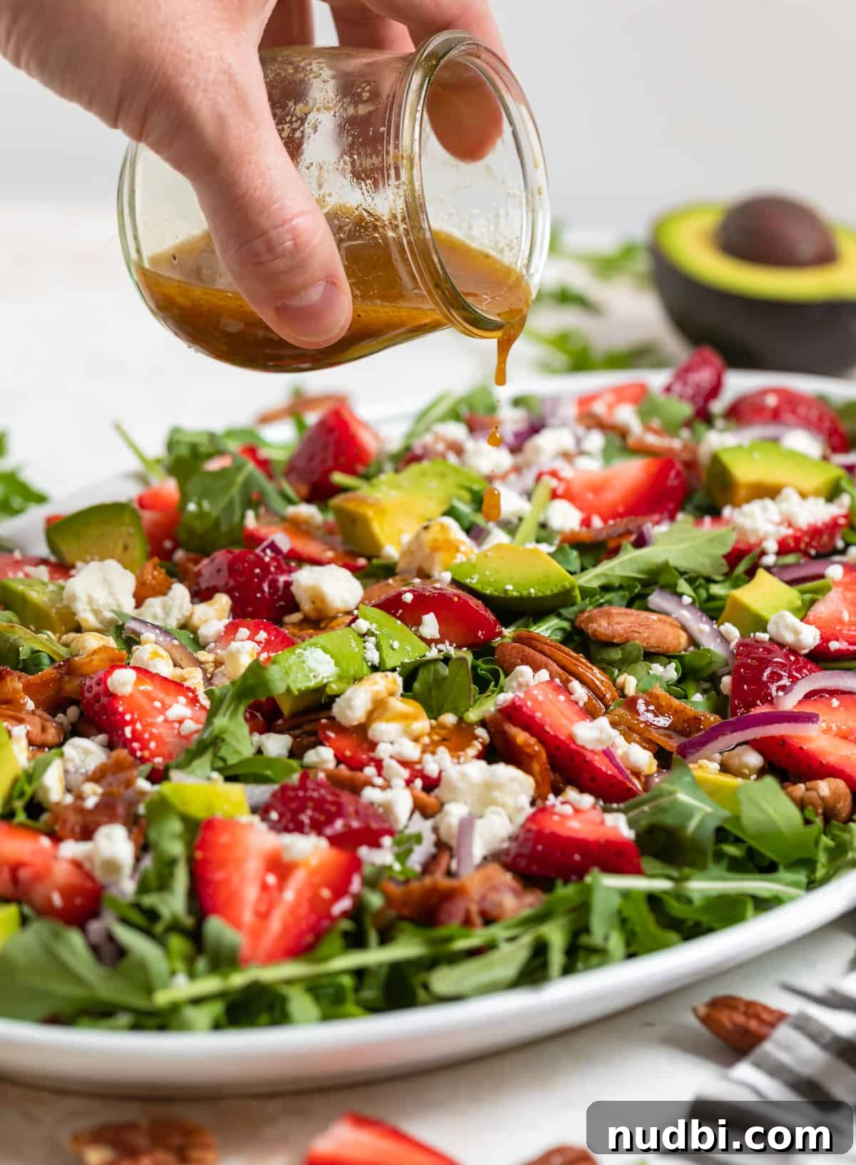 Strawberry and Goat Cheese Salad with Balsamic Glaze Recipe 3 Balsamic dressing being poured over strawberry goat cheese salad on white plate.