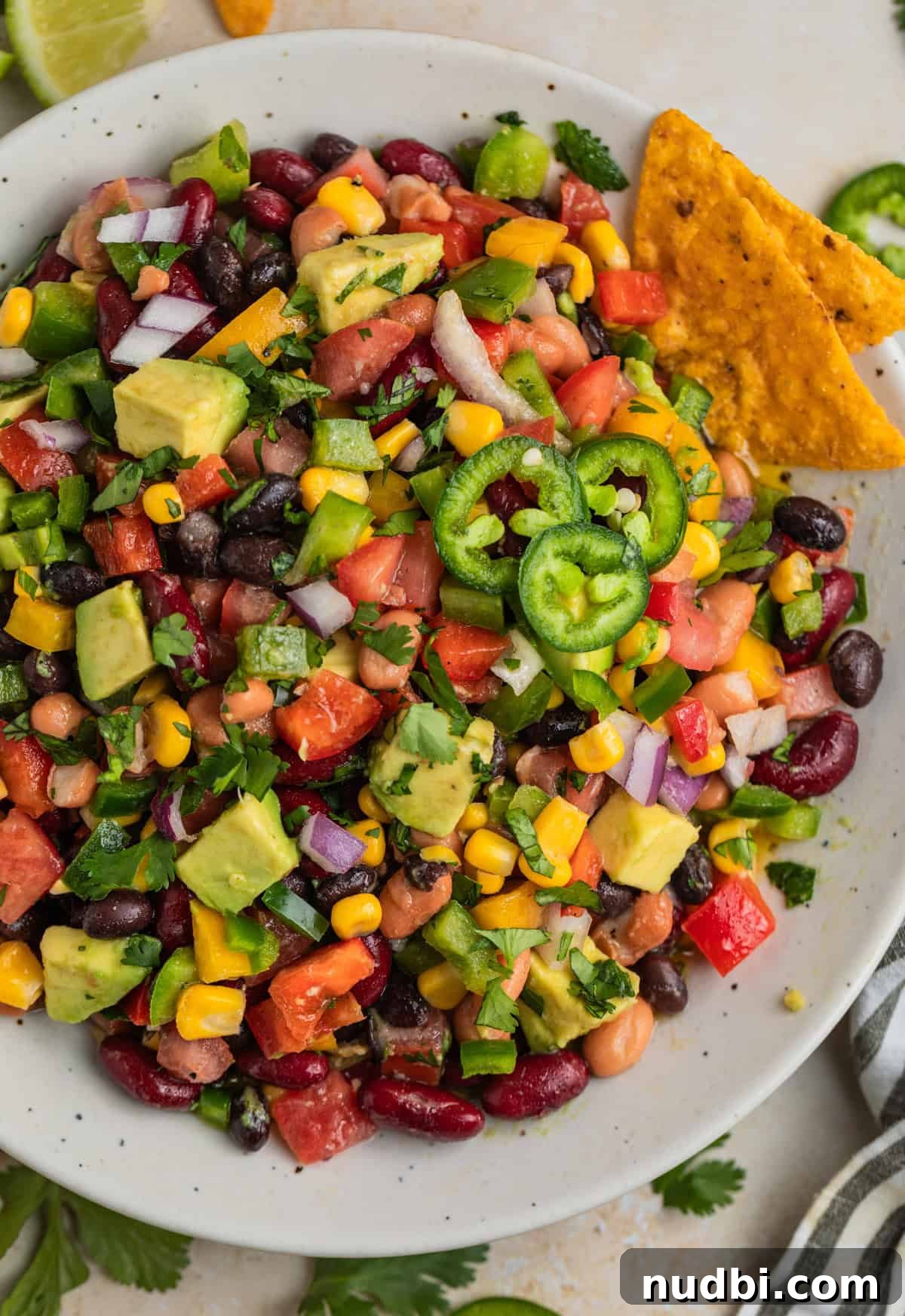 Southwestern Three-Bean, Corn & Avocado Salad Recipe 2 Overhead view of white bowl with 3 bean avocado corn salad topped with chopped cilantro.