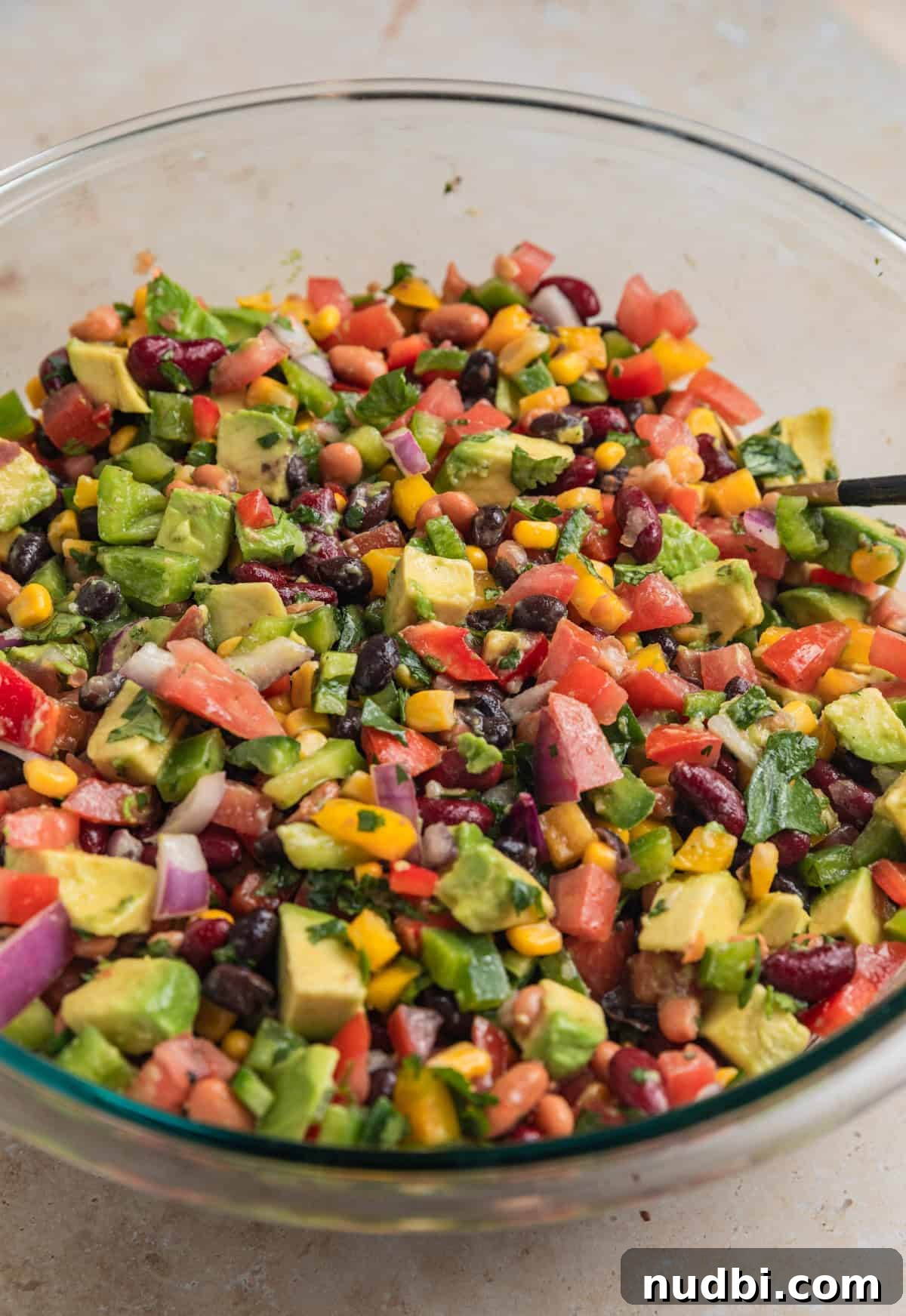 Southwestern Three-Bean, Corn & Avocado Salad Recipe 8 Bean corn and avocado salad mixed in mixing bowl with spoon.