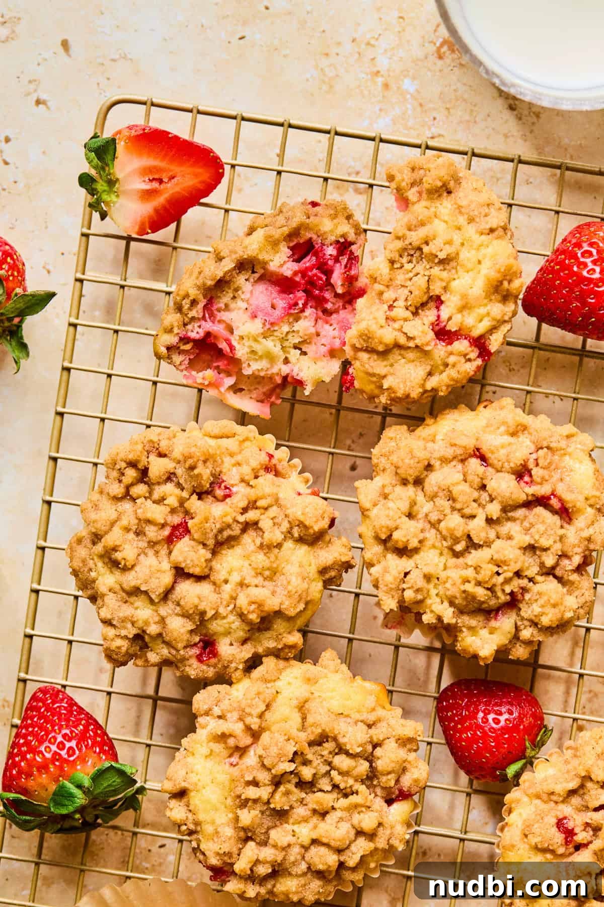 Strawberry Crumble Muffins: Moist Muffins with Crunchy Topping 14 Halved strawberry crumb muffin on muffin cup with berries and muffins around it.