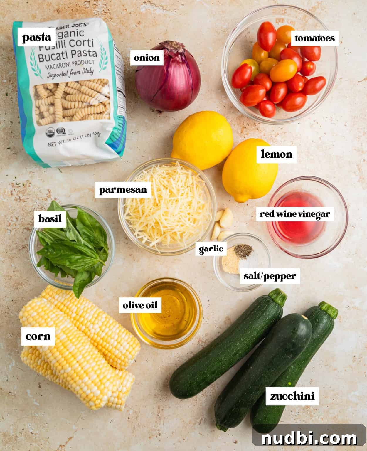 Grilled Zucchini Pasta Salad with Lemon Garlic Dressing 3 Lemons, tomatoes, corn, cheese, pasta and other ingredients labeled on surface.