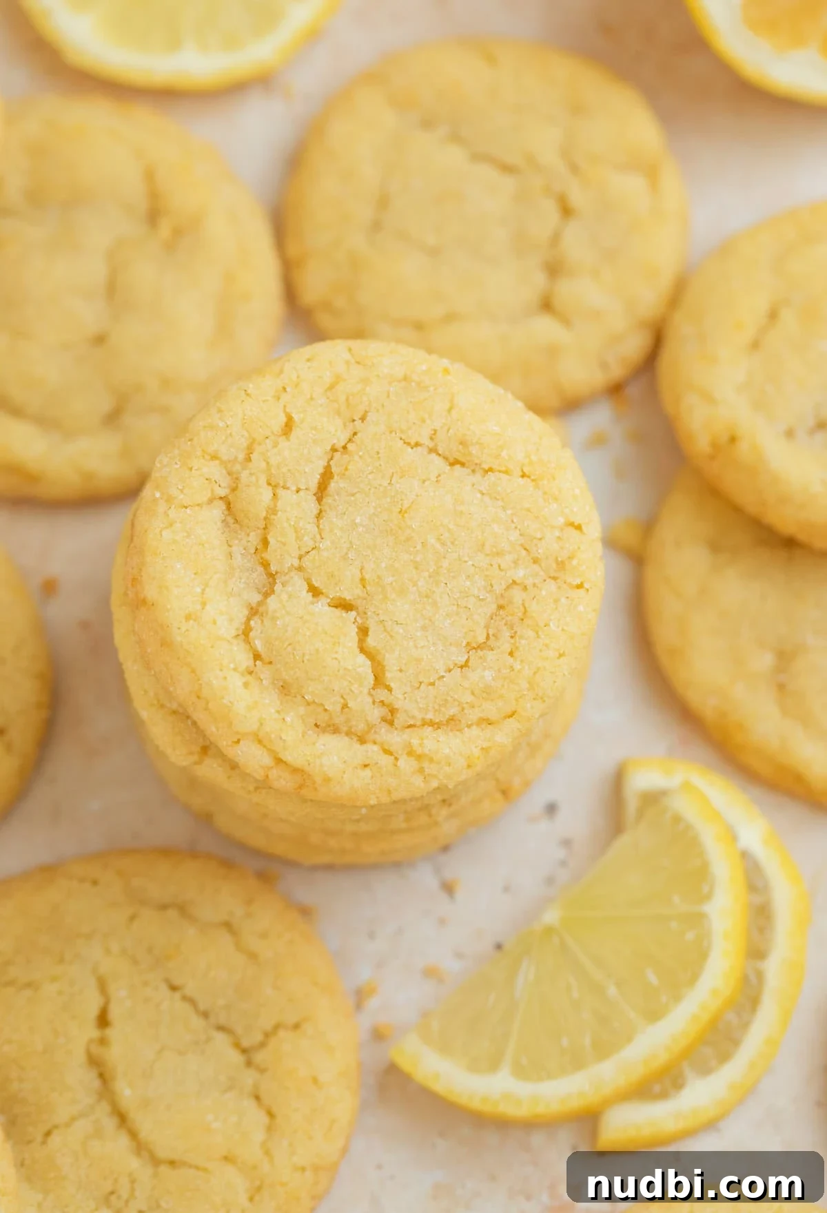 Zesty Lemon Sugar Cookies Recipe for Soft, Crispy Cookies 2 Stack of lemon sugar cookies next to lemon slices and other lemon cookies.