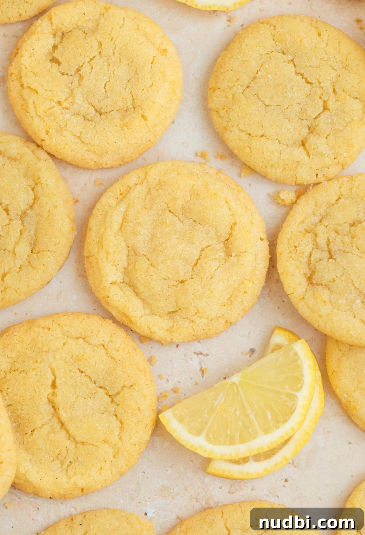 Zesty Lemon Sugar Cookies Recipe for Soft, Crispy Cookies 11 Lemon cookies on surface with lemon wedges and crumbs.