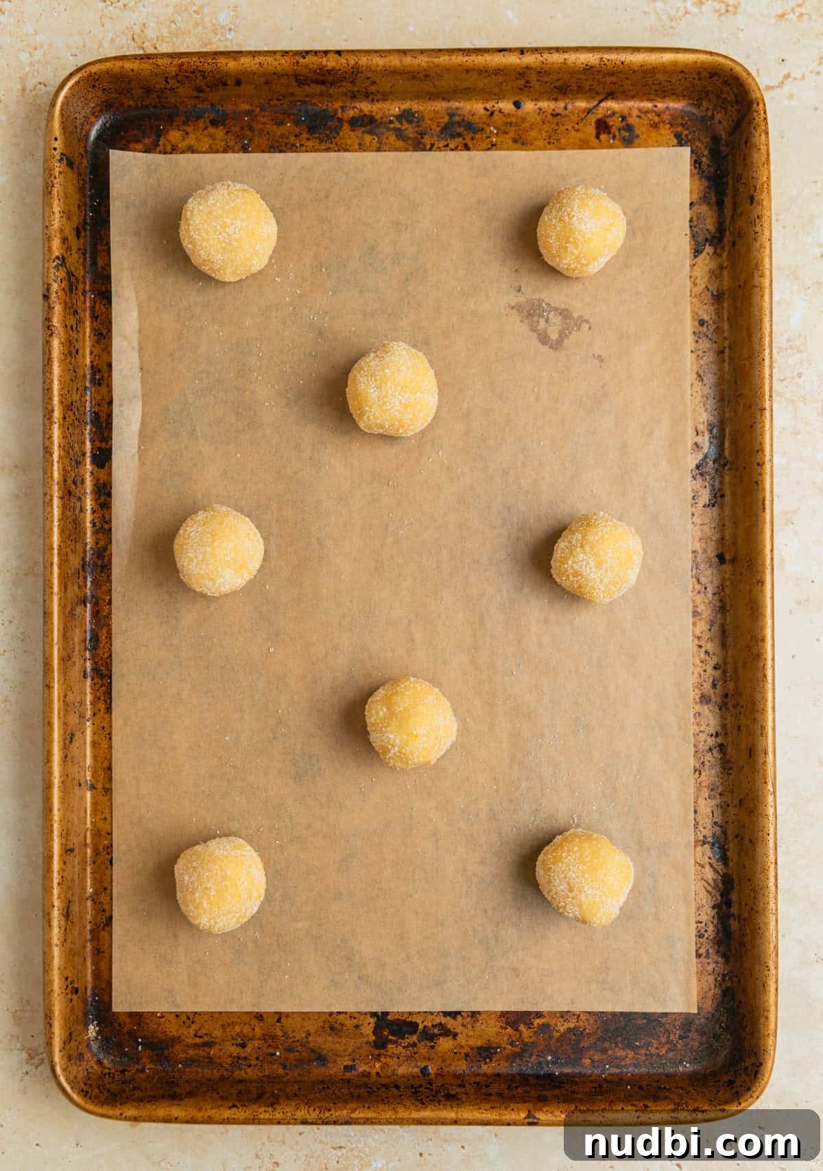 Zesty Lemon Sugar Cookies Recipe for Soft, Crispy Cookies 9 Rolled cookie dough balls rolled in sugar on parchment lined cookie sheet.