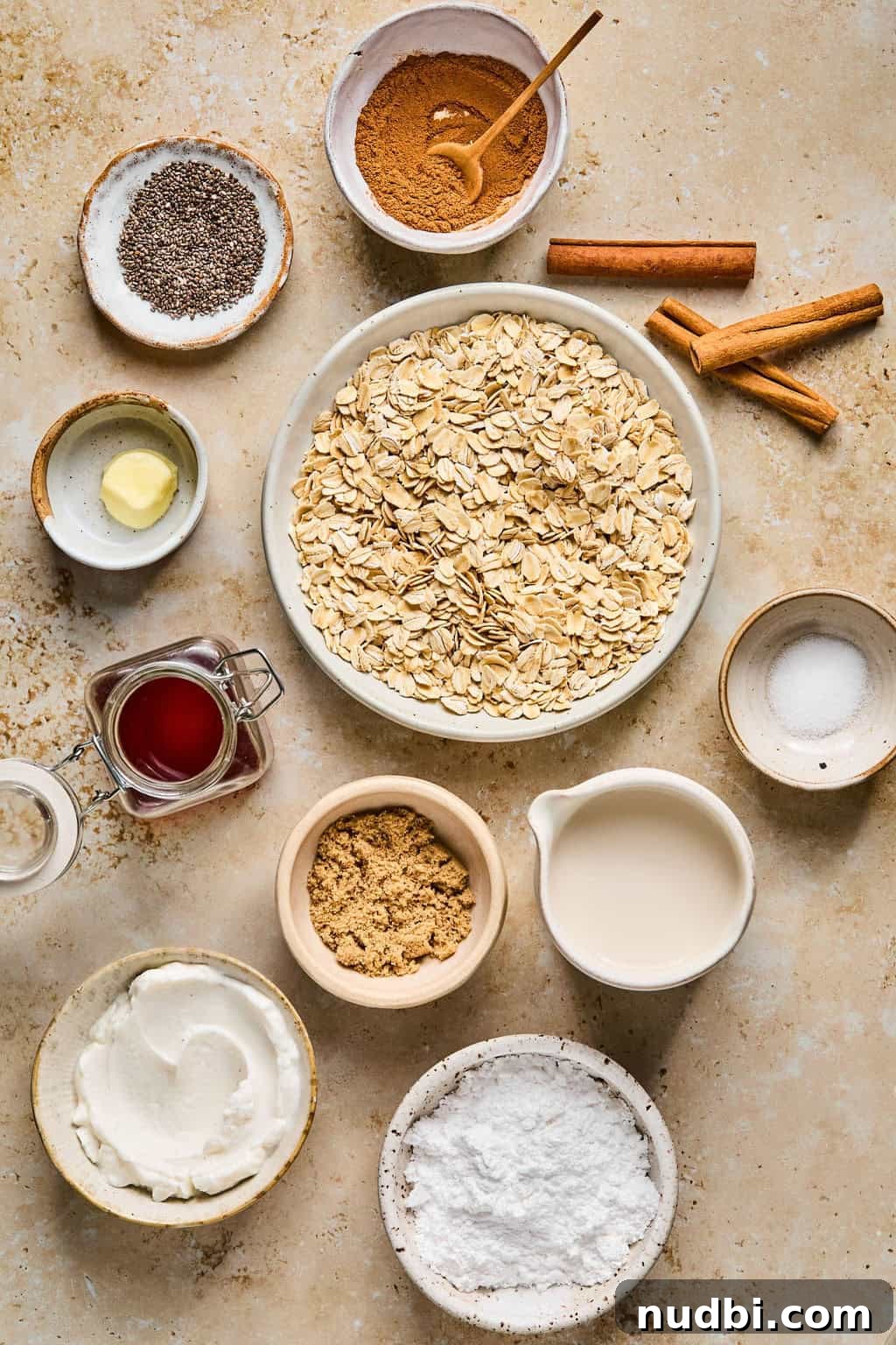 Cinnamon Roll Overnight Oats Recipe for Quick Morning Bliss 3 Rolled oats, vanilla yogurt, cinnamon sticks, vanilla and other ingredients arranged on surface.