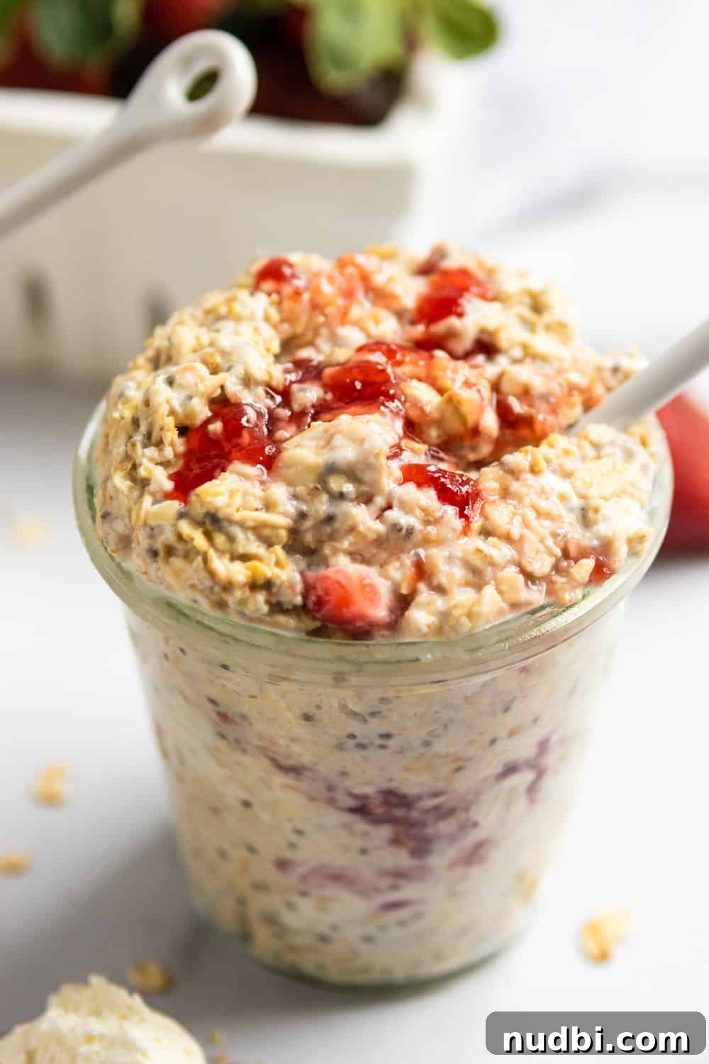 Strawberry Cheesecake Overnight Oats Recipe for Creamy Breakfast 2 Jar of strawberry cheesecake overnight oatmeal with white spoon and oats on counter surrounding.