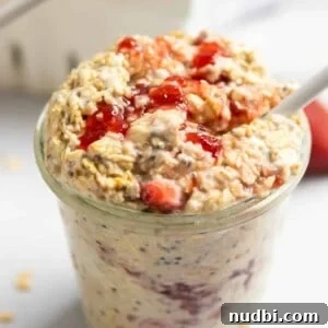 Strawberry Cheesecake Overnight Oats Recipe for Creamy Breakfast 5 Jar of strawberry cheesecake overnight oatmeal with white spoon and oats on counter surrounding.