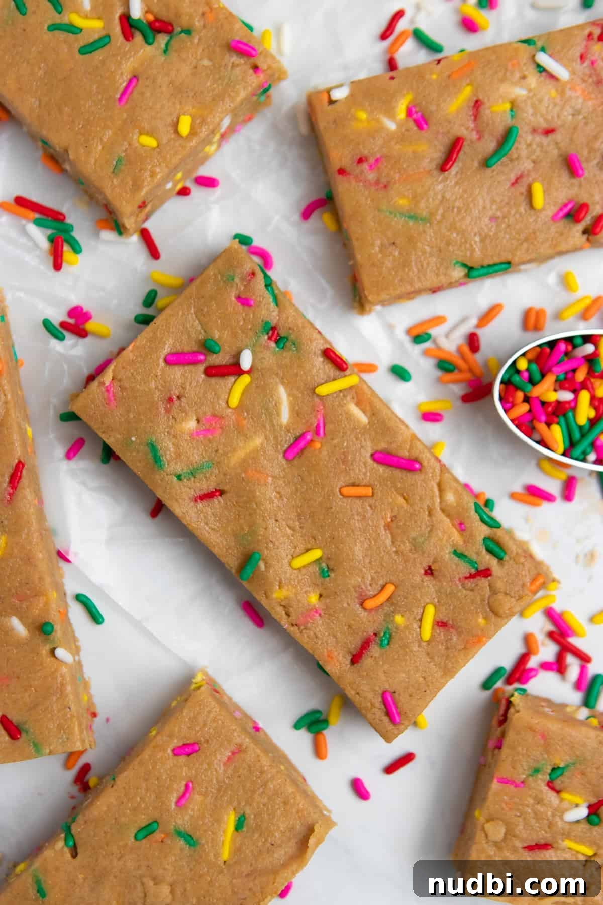 Birthday Cake Protein Bars Recipe — High-Protein Snack for Parties 2 No bake birthday cake protein bars on white counter with spoon of sprinkles.