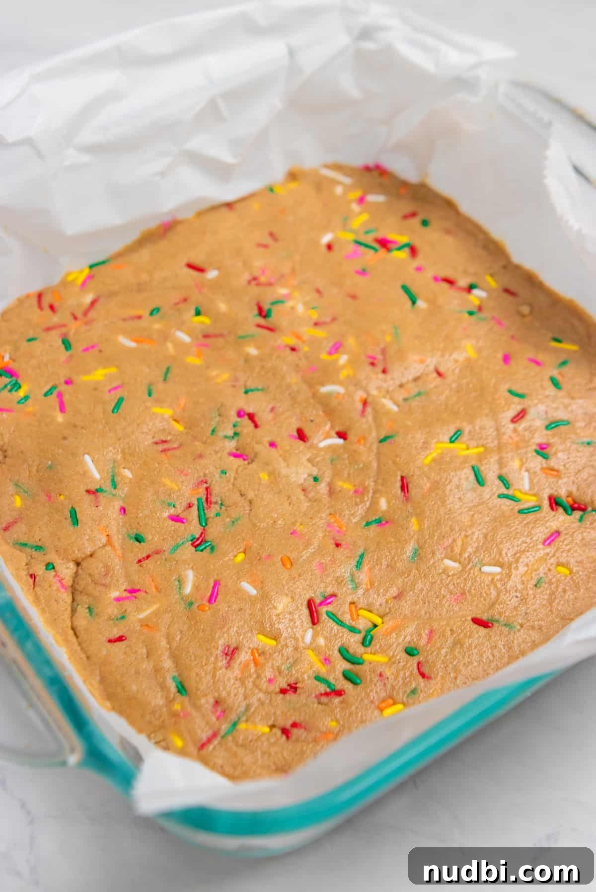 Birthday Cake Protein Bars Recipe — High-Protein Snack for Parties 6 Baking pan with no bake bars and rainbow sprinkles lined with parchment.