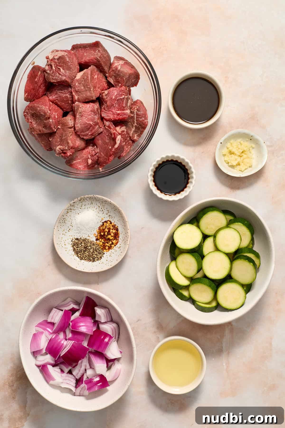 Grilled Steak Kabobs with Zesty Cilantro Chimichurri 4 Sirloin steak cubed in bowl, sliced zucchini, sliced red onion and other ingredients arranged on surface.