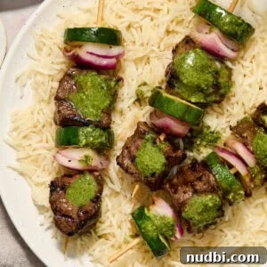 Grilled Steak Kabobs with Zesty Cilantro Chimichurri 6 Steak kabobs arranged on a plate over rice and topped with cilantro chimichurri.
