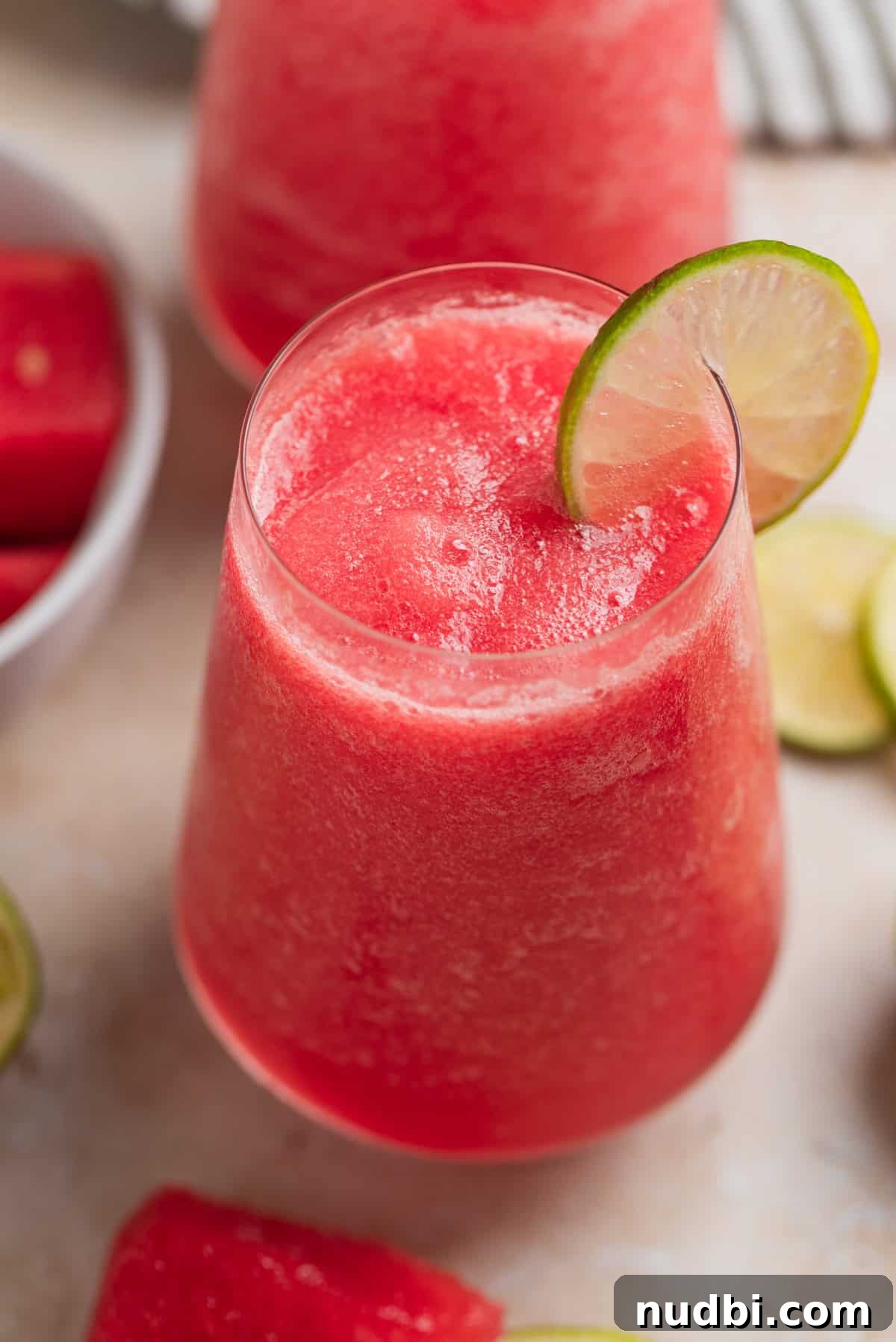 Watermelon Frosé Recipe: Frozen Rosé Cocktail for Summer 2 Watermelon frosé in glasses with lime slice and watermelon slices beside the glasses.