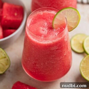 Watermelon Frosé Recipe: Frozen Rosé Cocktail for Summer 7 Stemless wine glass with watermelon rosé slushie or frosé with bowl of watermelon behind it as well as lime slices.