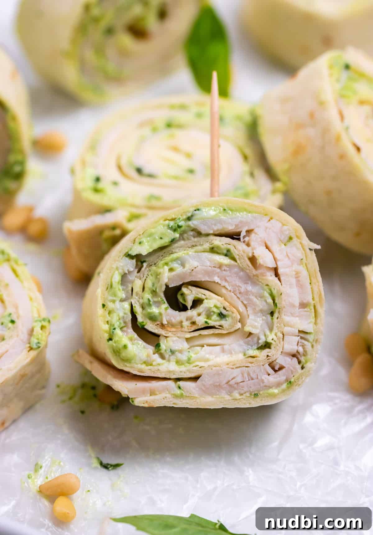 Smoked Provolone Turkey Pesto Pinwheels рецепт 2 Turkey pinwheels with cream cheese and pesto with toothpick on parchment.