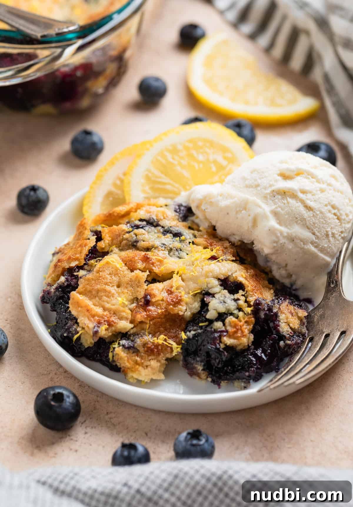 Lemon Blueberry Dump Cake Recipe for Quick Summer Desserts 2 Blueberry lemon dump cake on plate with vanilla ice cream scoop and lemon slices on plate.