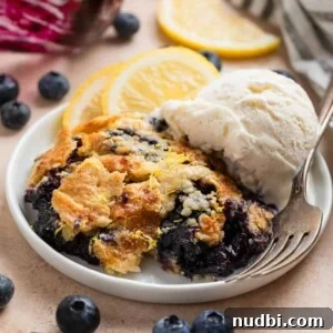 Lemon Blueberry Dump Cake Recipe for Quick Summer Desserts 11 Blueberry lemon dump cake on white plate with fork and scoop of vanilla ice cream.