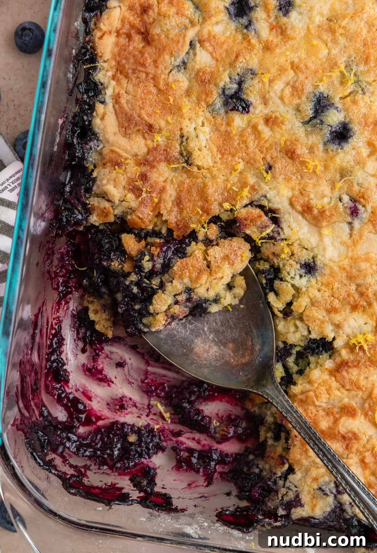 Lemon Blueberry Dump Cake Recipe for Quick Summer Desserts 9 Pan with blueberry dump cake and serving spoon scooping up part with lemon zest over top.