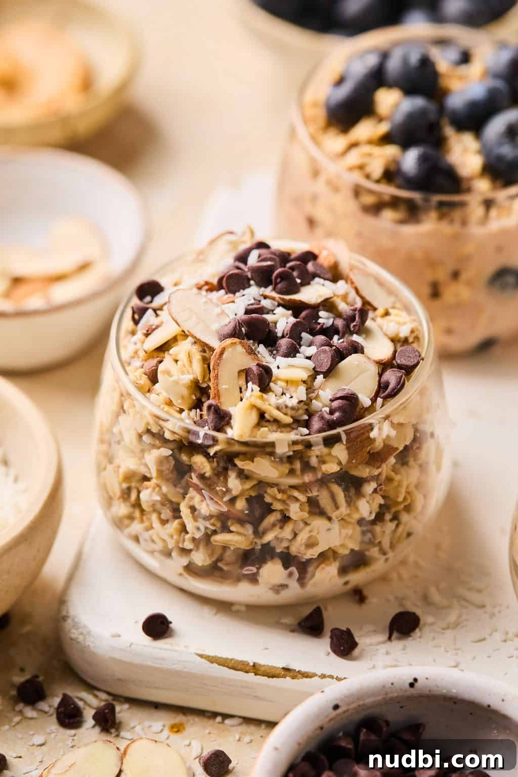 6 Overnight Oats Recipes for Quick, Nutritious Breakfasts 11 Almond, coconut and chocolate chip oats in glass with other dishes surrounding.
