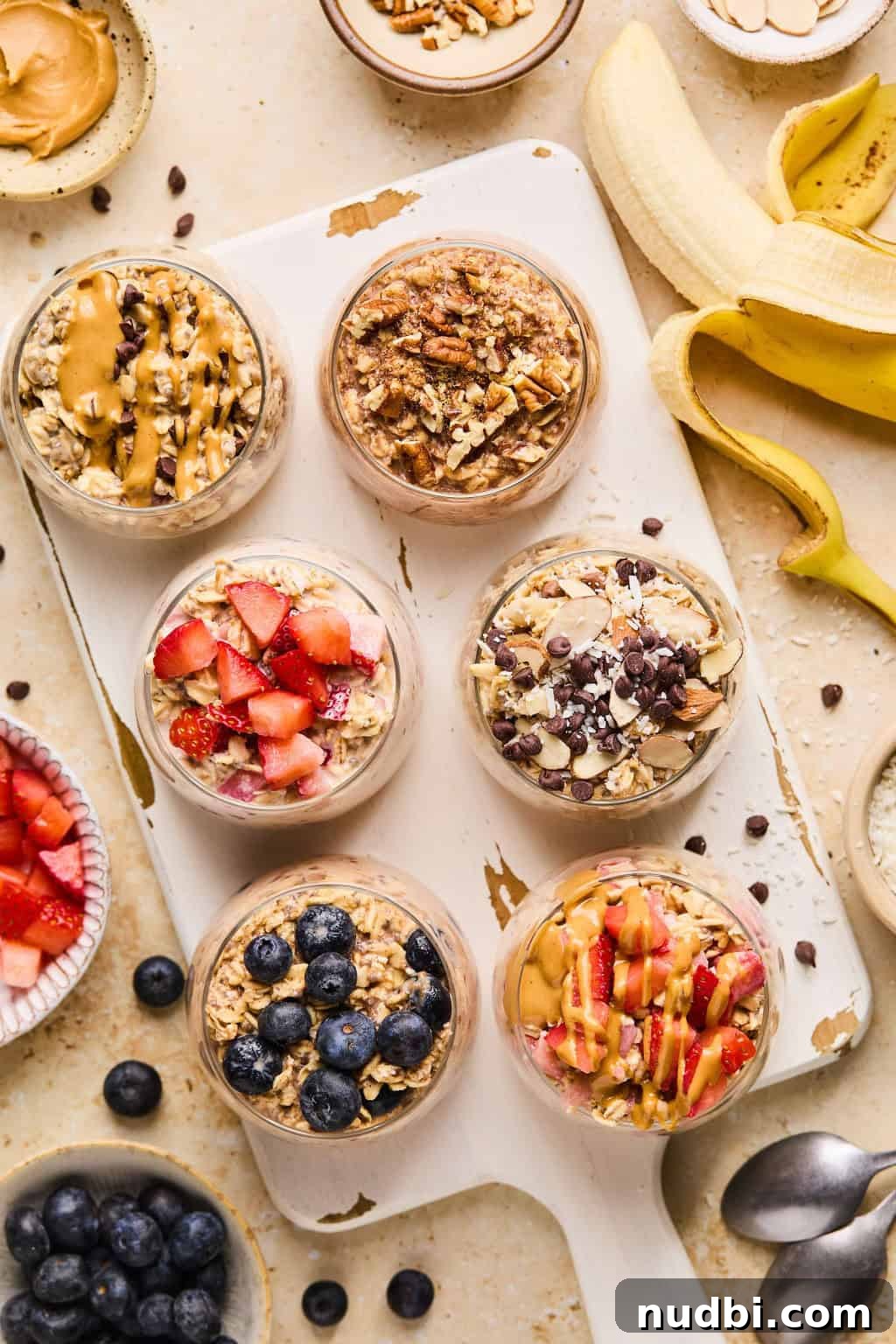 6 Overnight Oats Recipes for Quick, Nutritious Breakfasts 3 Oatmeal prepared in glasses on white cutting board and topped with berries, chocolate chips, peanut butter, etc.