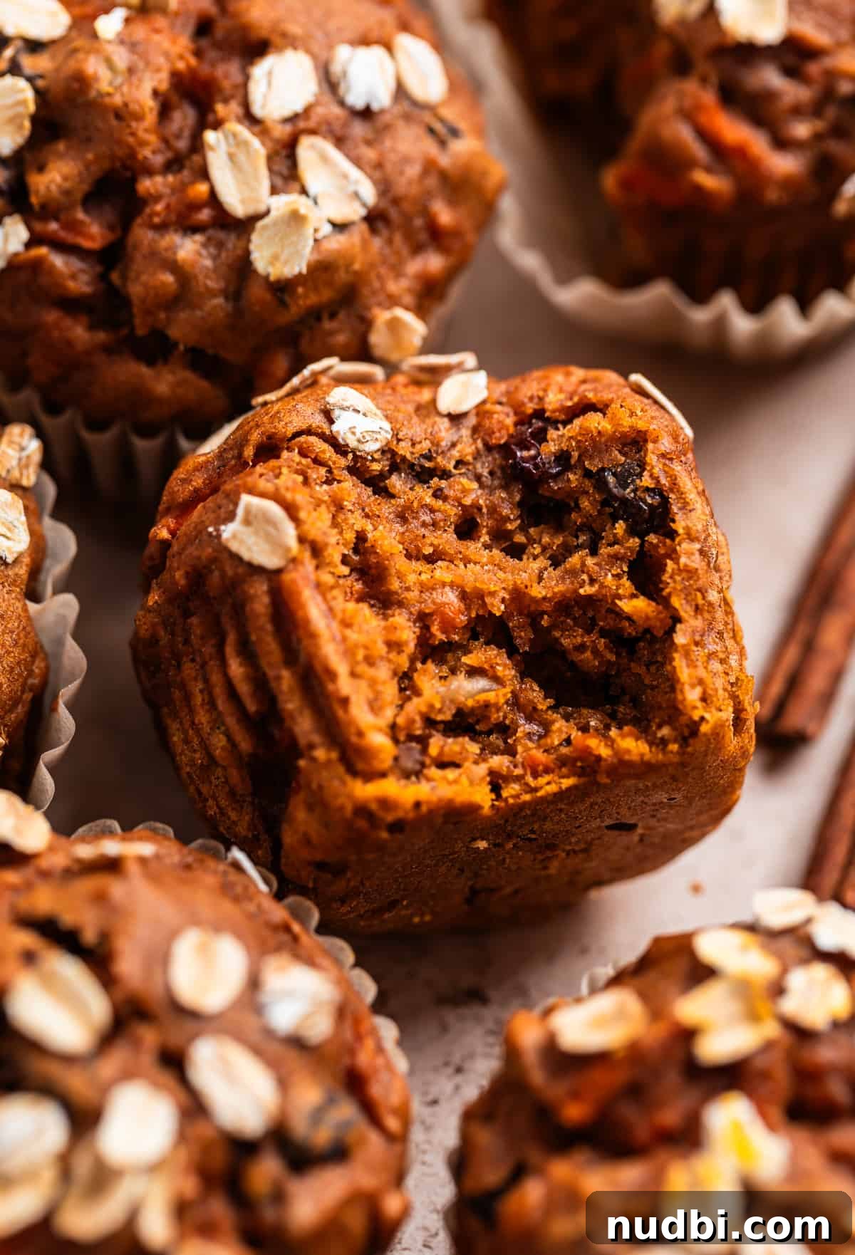 Moist Pumpkin and Carrot Muffins with Warm Spices 3 Bite shot of pumpkin carrot muffin surrounded by other muffins and two cinnamon sticks.