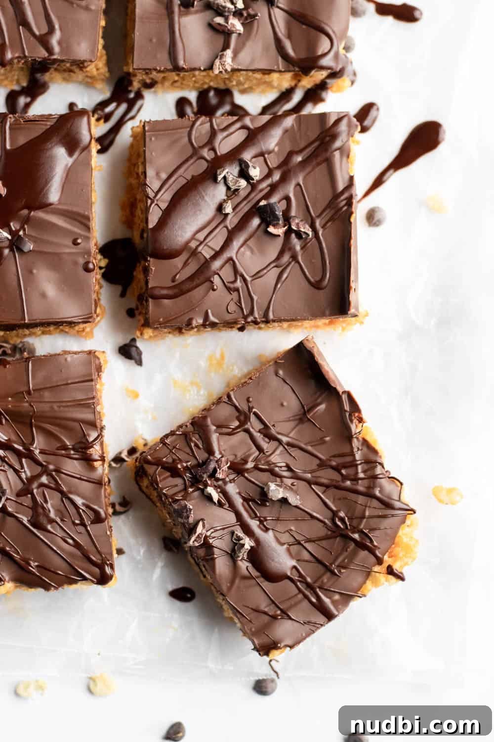 Chocolate Peanut Butter Rice Krispie Treats Recipe 2 Chocolate peanut butter rice krispie treats with chocolate drizzle and chocolate chips on parchment.