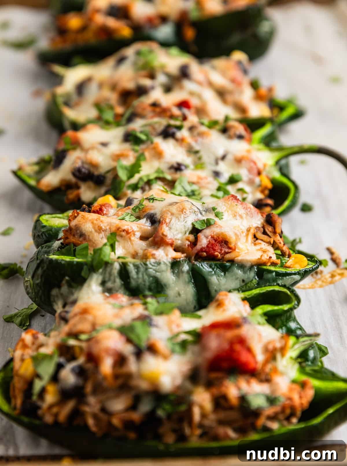 Chicken-Stuffed Poblano Peppers with Savory Cheese Filling 3 Chicken stuffed poblano peppers lined on baking sheet topped with cilantro and cheese.