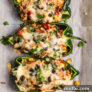 Chicken-Stuffed Poblano Peppers with Savory Cheese Filling 10 Chicken stuffed poblano peppers on parchment topped with cheese and cilantro.
