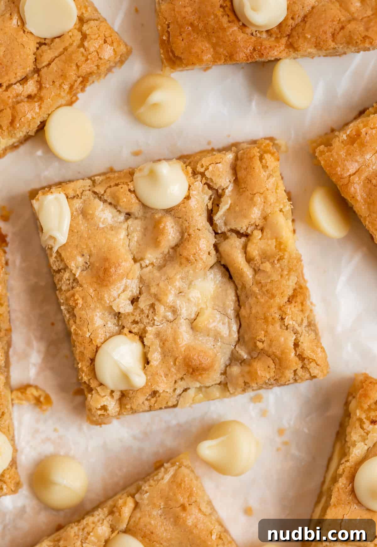 Chewy Gluten-Free Blondies Recipe That Melts in Your Mouth 8 Gluten free blondies with white chocolate chips arranged on parchment.