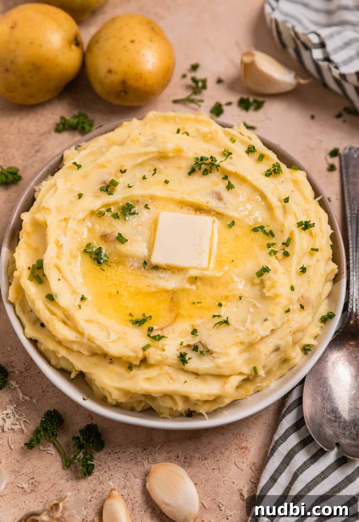 Garlic Parmesan Mashed Potatoes Made in the Instant Pot 3 Garlic parmesan mashed potatoes in bowl surrounded by garlic cloves, parsley and other ingredients.